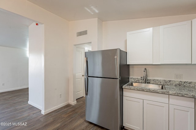 kitchen with a sink, visible vents, white cabinets, freestanding refrigerator, and dark wood finished floors