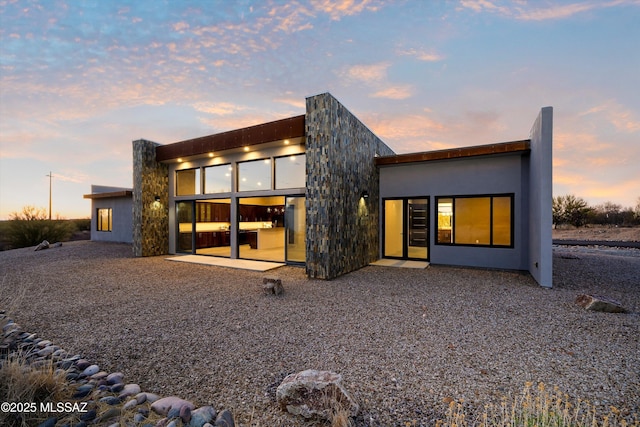 back of house at dusk featuring a patio area and stucco siding