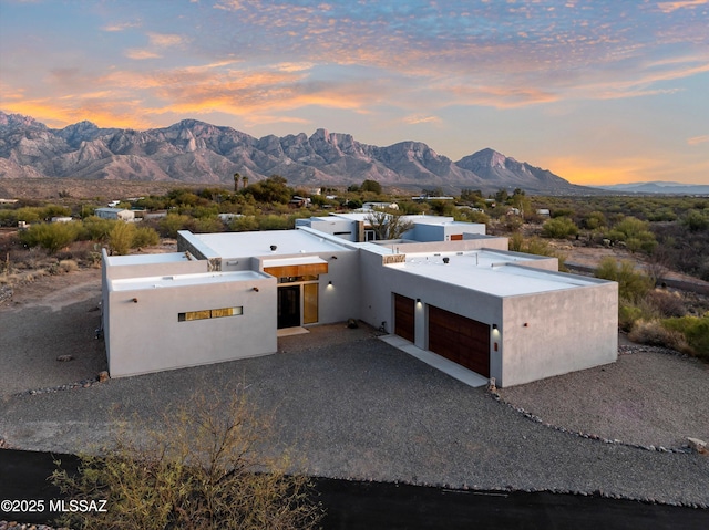 pueblo-style home featuring a garage, a mountain view, driveway, and stucco siding