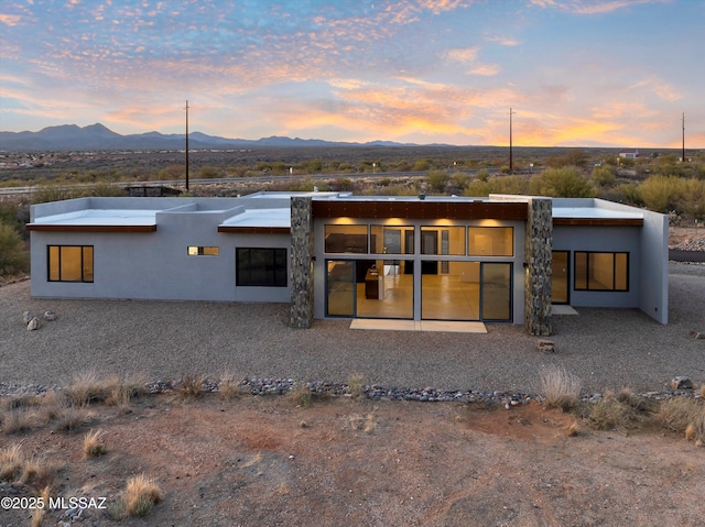 back of house at dusk with a mountain view and stucco siding