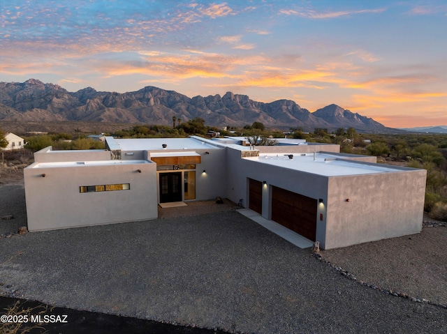 pueblo revival-style home with stucco siding, a mountain view, an attached garage, and gravel driveway