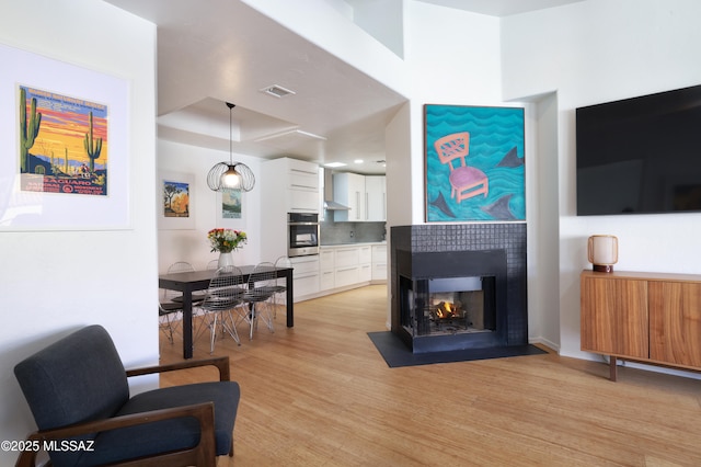 living room with light wood-type flooring, a multi sided fireplace, and visible vents