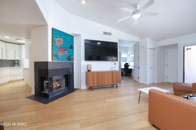 living area with visible vents, a ceiling fan, lofted ceiling, light wood-style floors, and a multi sided fireplace