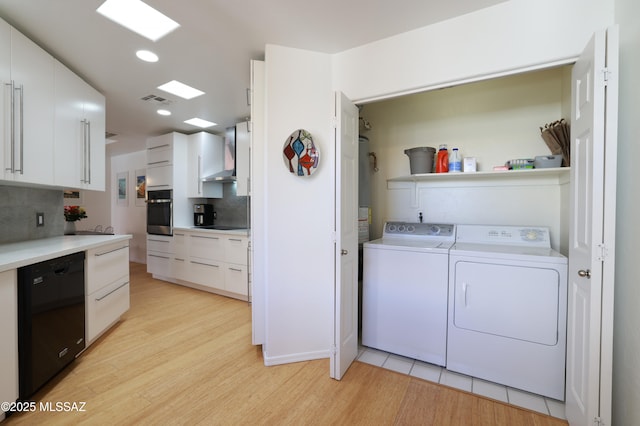 clothes washing area with laundry area, light wood finished floors, washing machine and clothes dryer, and visible vents