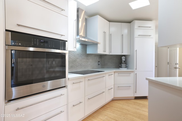 kitchen featuring white cabinets, decorative backsplash, wall chimney exhaust hood, oven, and black electric cooktop