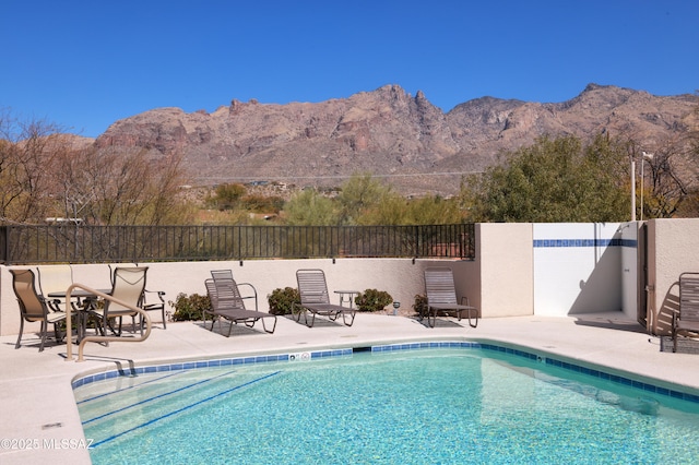 community pool with fence, a mountain view, and a patio