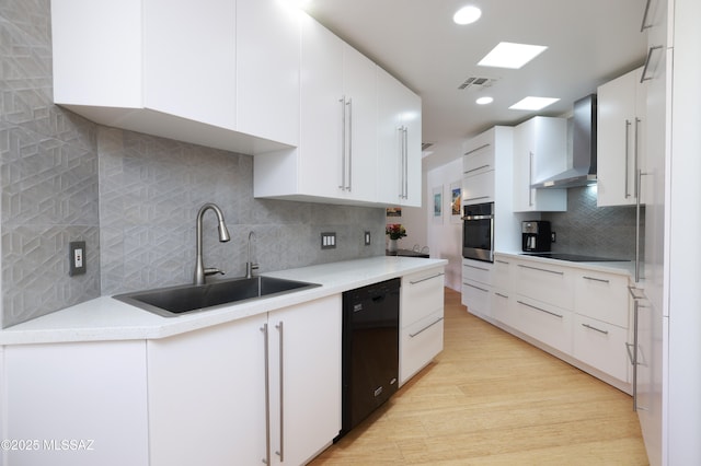 kitchen with a sink, visible vents, black appliances, light wood-type flooring, and wall chimney exhaust hood