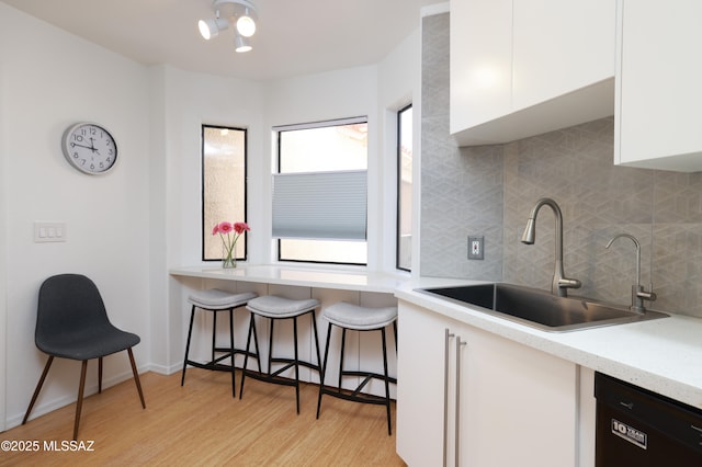 kitchen with light wood-style flooring, a sink, white cabinetry, light countertops, and dishwasher