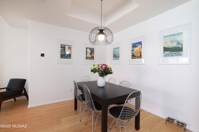 dining room featuring a tray ceiling, baseboards, and light wood finished floors