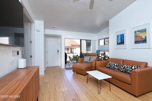 living area featuring lofted ceiling, light wood-style flooring, and a ceiling fan