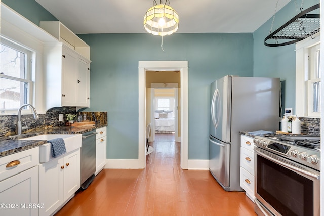 kitchen featuring stainless steel appliances, a sink, white cabinetry, tasteful backsplash, and dark stone countertops