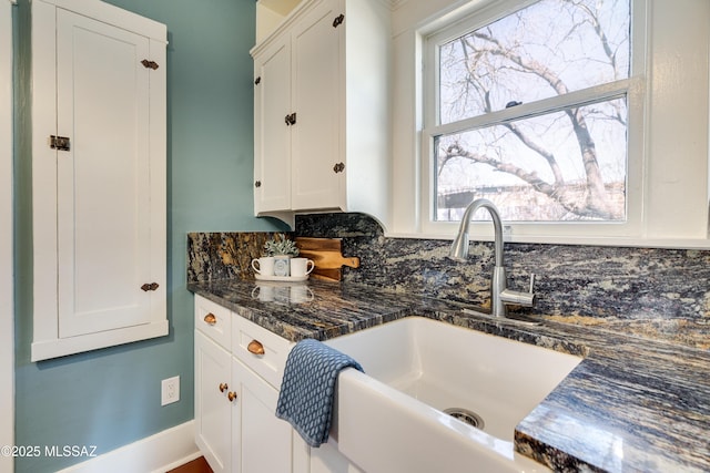 kitchen with baseboards, dark stone countertops, a sink, and white cabinets