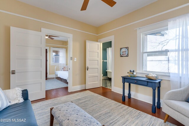 living area featuring dark wood-type flooring, ceiling fan, and baseboards