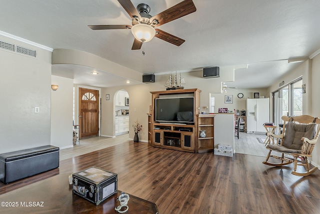 living room featuring arched walkways, crown molding, visible vents, ceiling fan, and wood finished floors