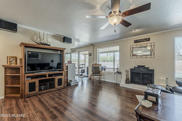 living area with baseboards, crown molding, a ceiling fan, and dark wood-style flooring