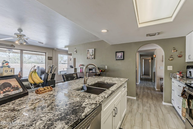 kitchen with arched walkways, a sink, white cabinetry, and light stone countertops