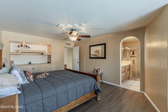 bedroom with baseboards, visible vents, connected bathroom, arched walkways, and wood finished floors