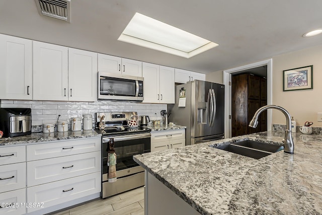 kitchen with light stone counters, tasteful backsplash, visible vents, appliances with stainless steel finishes, and a sink