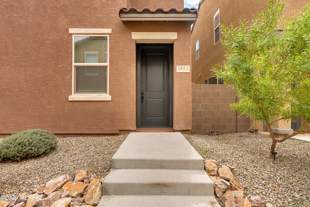 doorway to property with a tile roof, fence, and stucco siding