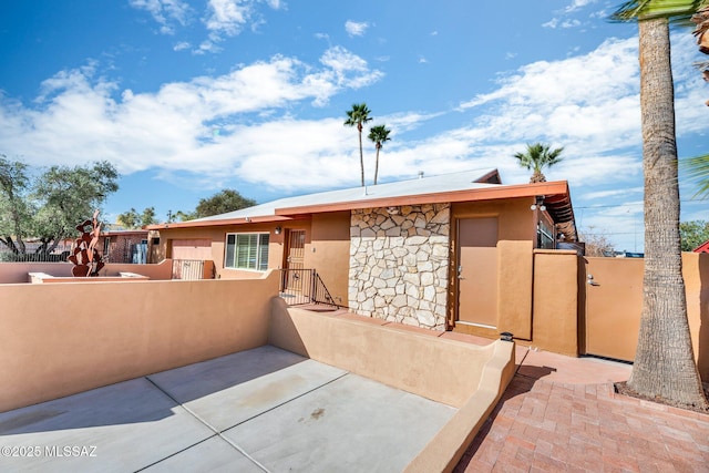 view of front facade with a gate, stone siding, fence, and stucco siding