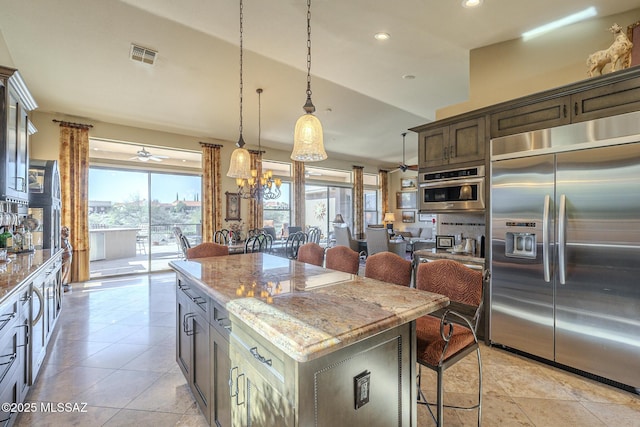 kitchen featuring visible vents, appliances with stainless steel finishes, a breakfast bar, light stone counters, and a center island