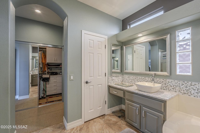 bathroom with tasteful backsplash, a walk in closet, vanity, and baseboards