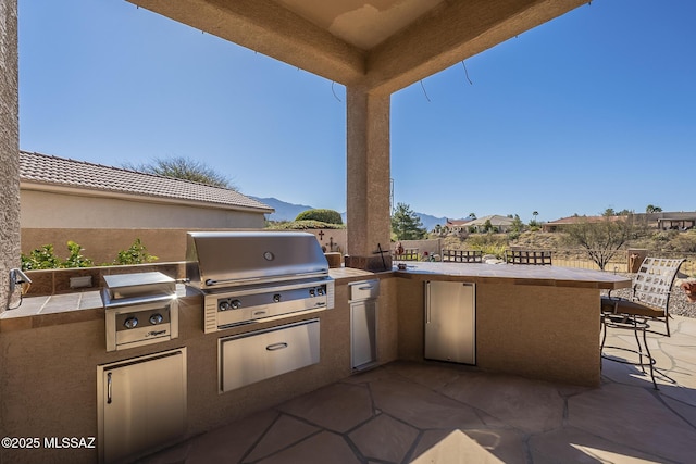 view of patio / terrace featuring an outdoor kitchen, fence, grilling area, and outdoor wet bar