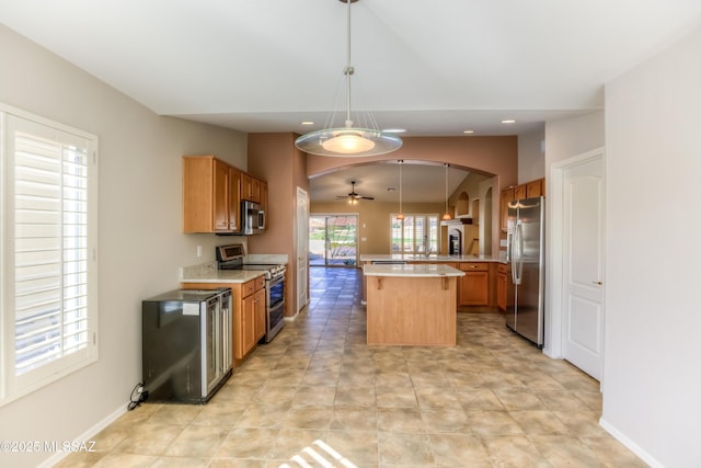 kitchen featuring arched walkways, a ceiling fan, a center island, stainless steel appliances, and light countertops