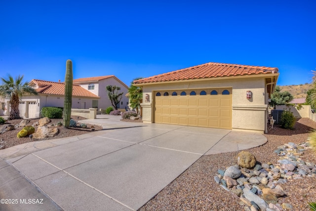 mediterranean / spanish house with concrete driveway, a tiled roof, an attached garage, central AC, and stucco siding