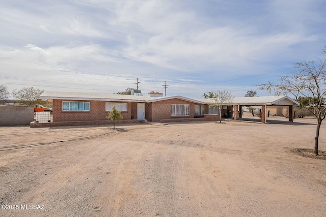 ranch-style house with dirt driveway, fence, a carport, and brick siding