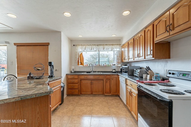 kitchen featuring brown cabinetry, white appliances, a healthy amount of sunlight, and a sink