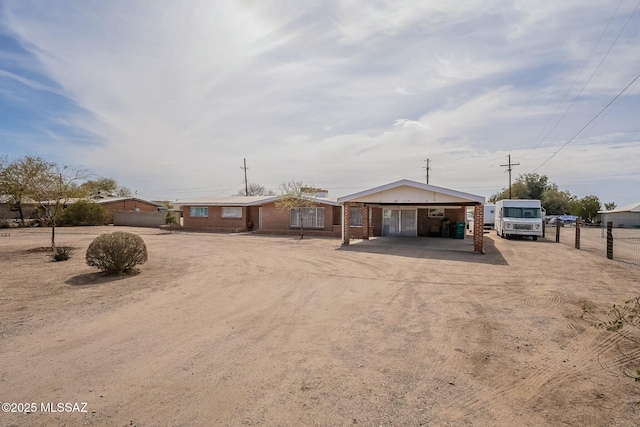 view of front facade featuring dirt driveway, a carport, brick siding, and fence