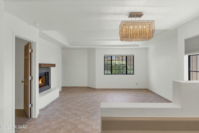 unfurnished living room featuring a lit fireplace, a raised ceiling, and tile patterned floors