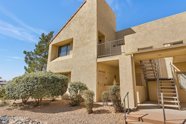 view of property exterior featuring stucco siding, a balcony, and stairs