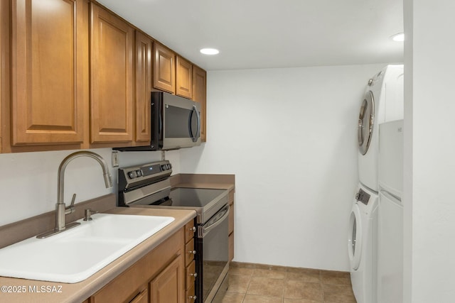 kitchen with brown cabinets, light tile patterned floors, stainless steel appliances, a sink, and stacked washing maching and dryer