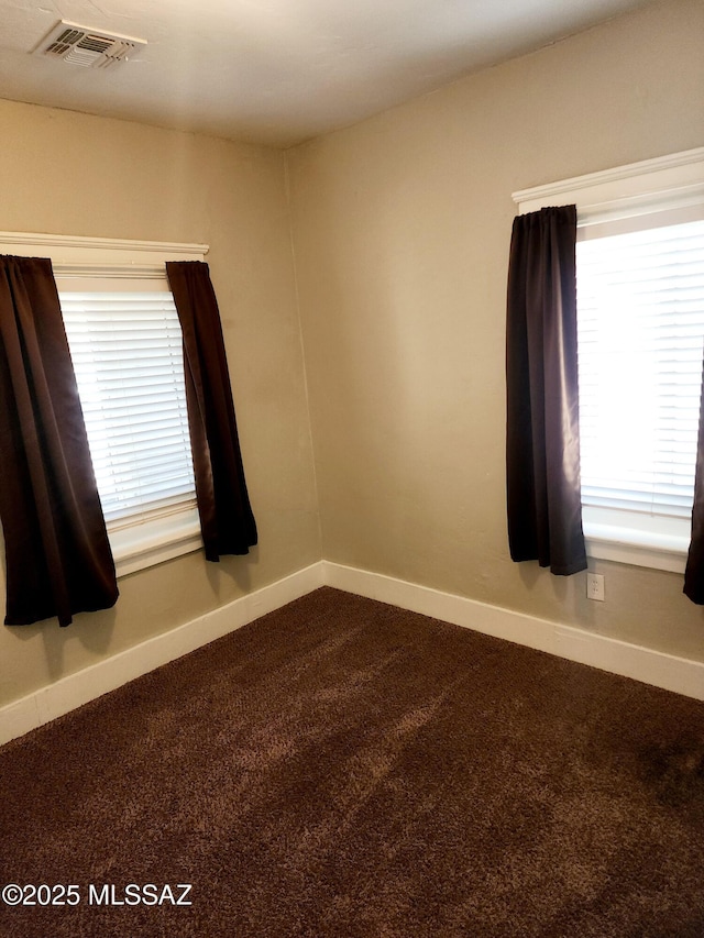 empty room with dark colored carpet, visible vents, and baseboards