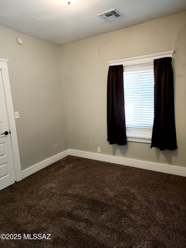 unfurnished room with baseboards, visible vents, and dark carpet