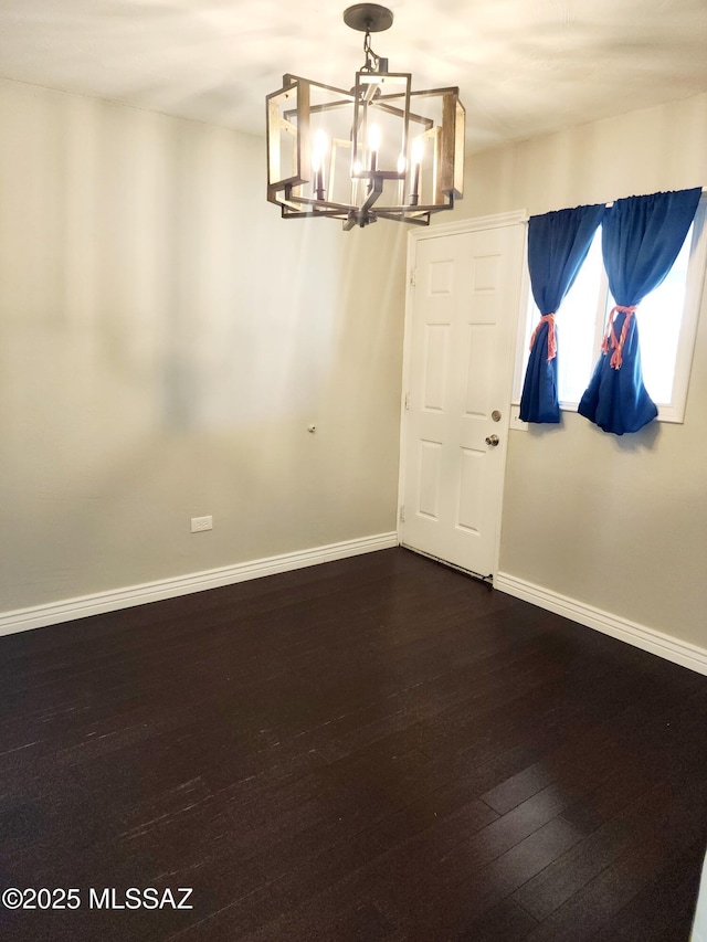 unfurnished room featuring dark wood-style floors, baseboards, and a notable chandelier