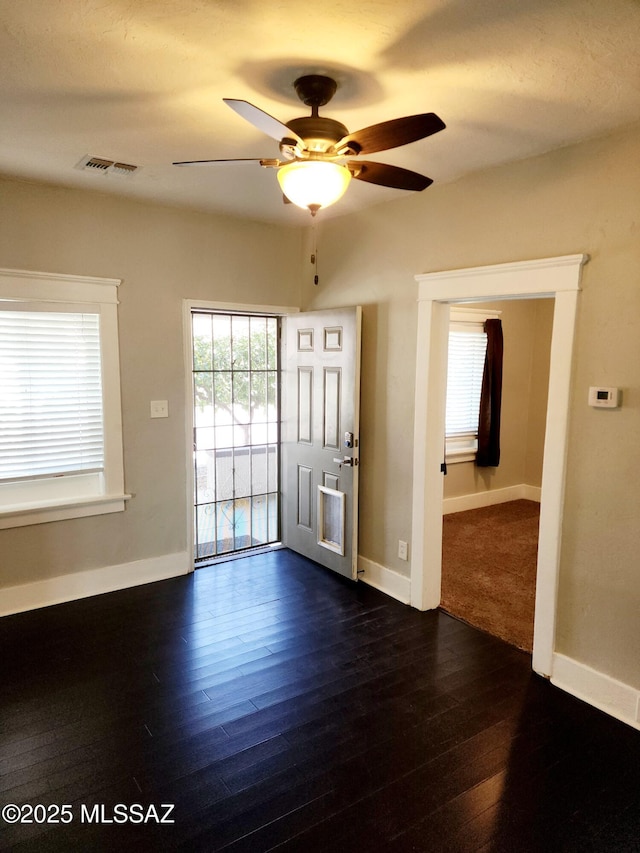 empty room with dark wood-style floors, ceiling fan, visible vents, and baseboards