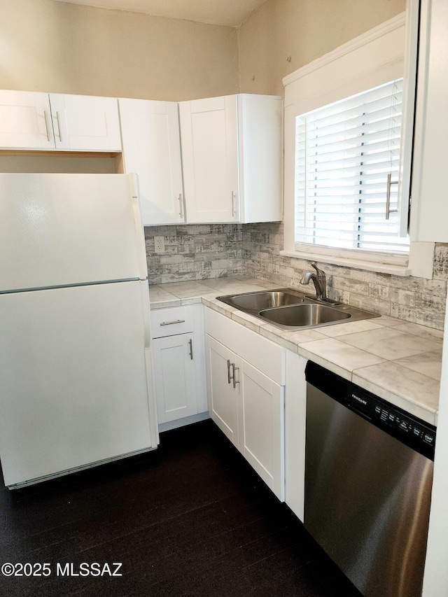 kitchen featuring a sink, white cabinets, stainless steel dishwasher, backsplash, and freestanding refrigerator