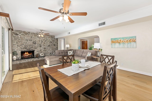 dining room featuring arched walkways, a stone fireplace, wood finished floors, visible vents, and baseboards