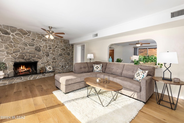 living area with visible vents, arched walkways, wood finished floors, and a stone fireplace