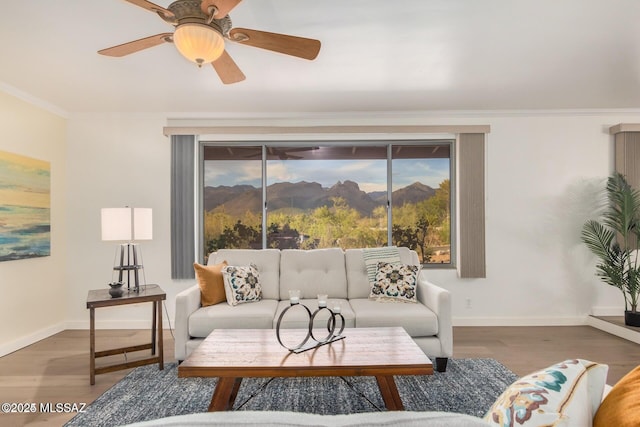 living area with a ceiling fan, baseboards, ornamental molding, and wood finished floors