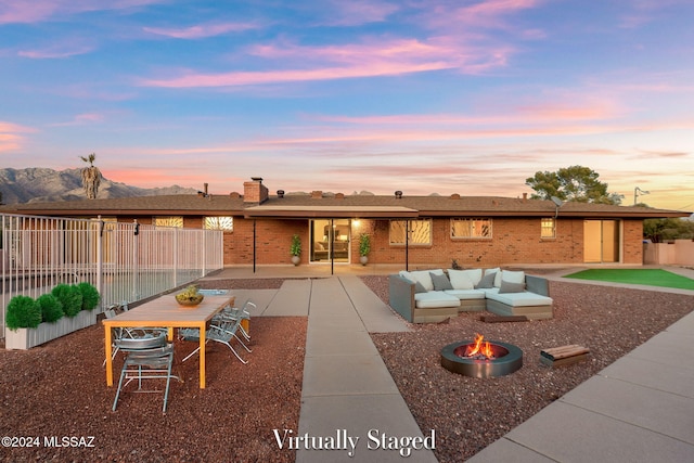 back of property at dusk with brick siding, an outdoor living space with a fire pit, fence, and a patio