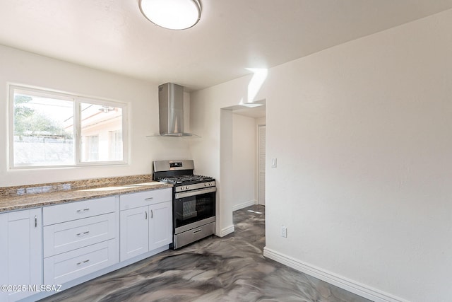 kitchen with baseboards, white cabinets, gas range, finished concrete floors, and wall chimney range hood