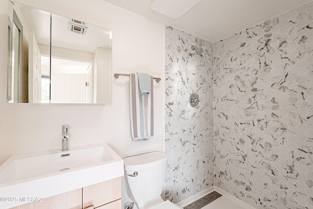 bathroom featuring toilet, visible vents, a tile shower, and vanity