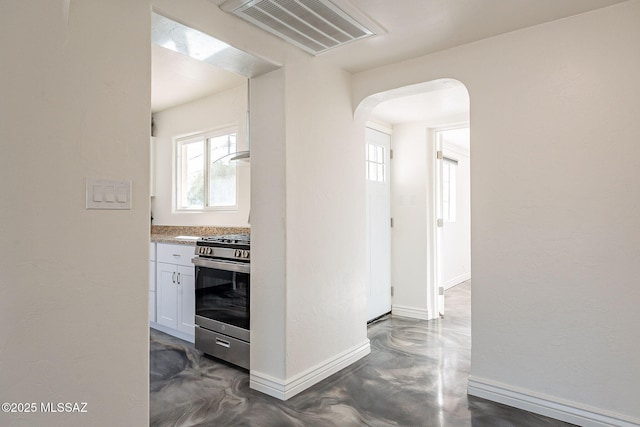 hallway with arched walkways, baseboards, visible vents, and finished concrete floors