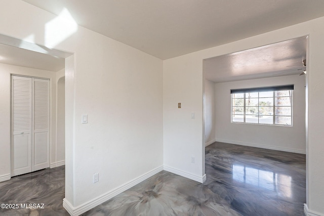 spare room featuring arched walkways, finished concrete floors, a ceiling fan, and baseboards