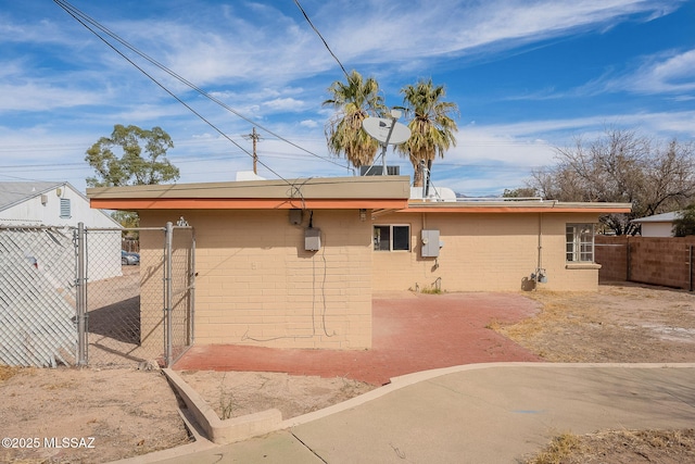 back of property with concrete block siding, a gate, fence, and a patio