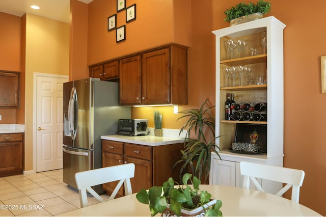 kitchen with light tile patterned floors, light countertops, a towering ceiling, brown cabinetry, and stainless steel fridge with ice dispenser